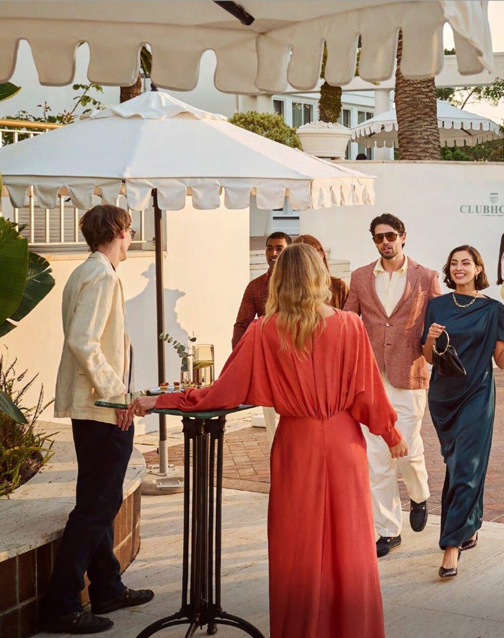 Guests arriving at a clubhouse terrace in the early evening, scalloped parasols and palms; illustrative photograph.
